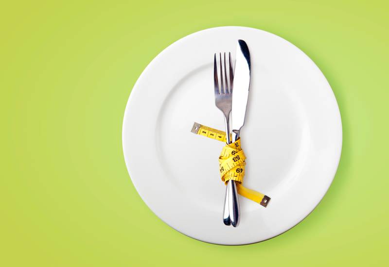 plate with a knife and fork wrapped in a measuring tape on top