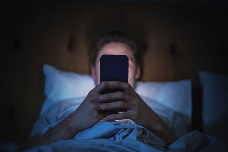 man in bed staring at cellphone screen