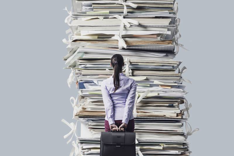 woman standing in fron of huge paperwork pile