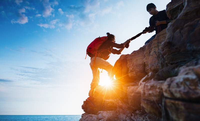 rock climbers helping each other up precarious area